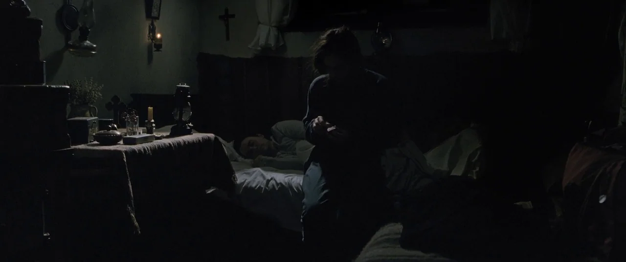 Beyond the Hills (2012) movie still: medium — A dimly lit room with rustic furniture and a small wooden crucifix on the wall. A woman sits on the…