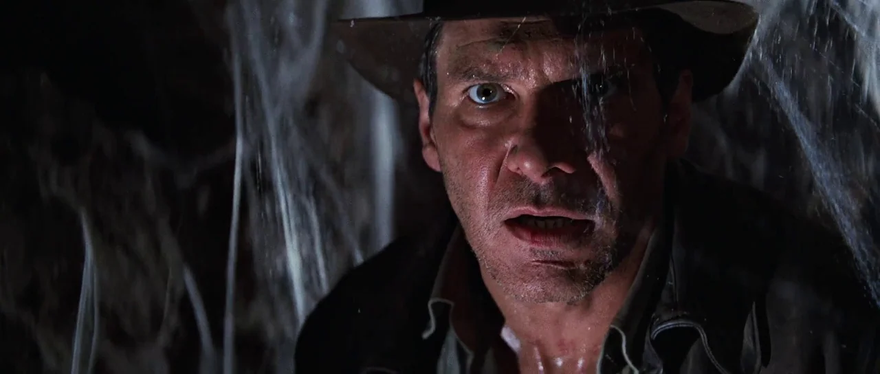 Indiana Jones and the Last Crusade (1989) movie still: closeup — A dark, cramped space filled with thick, hanging spiderwebs in the foreground and…