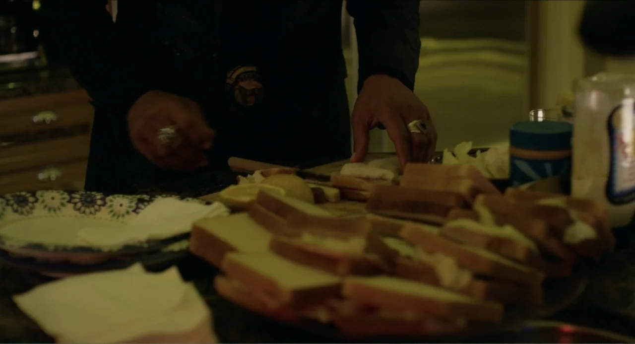 Instantes Capturados (2022) movie still: medium — A dark kitchen counter is covered with numerous prepared sandwiches and paper plates. A man in a…