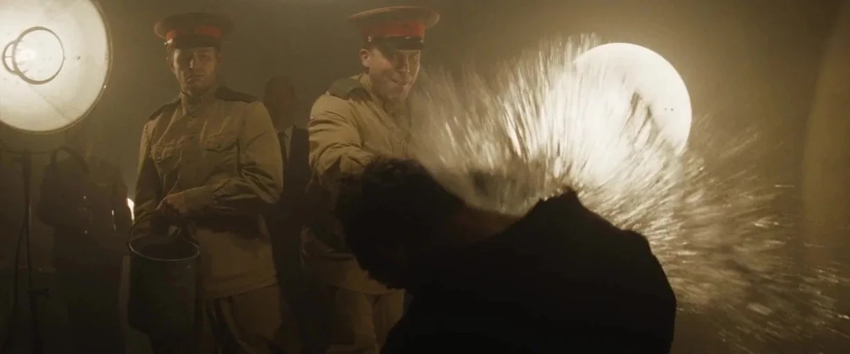 Bridge of Spies (2015) movie still: medium — A dimly lit room with walls obscured by thick, hazy smoke. One man throws a bucket of water at another…