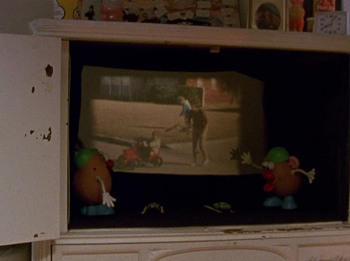 Slacker (1991) movie still: medium — A miniature toy television set acts as a projection screen for a home movie. Two plastic potato toys flank the…