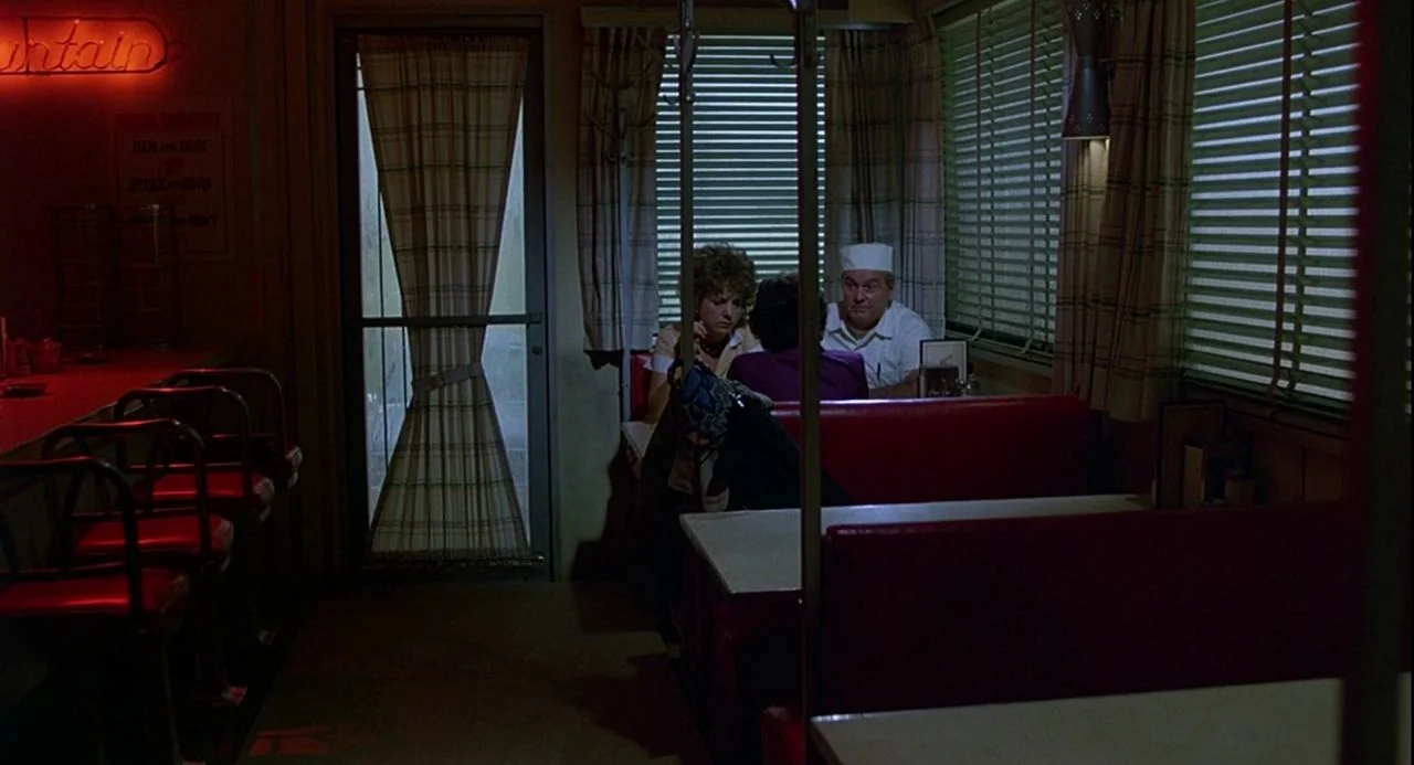 Psycho III (1986) movie still: wide — A dimly lit restaurant interior features red vinyl booths and venetian blinds on windows. Three individuals…