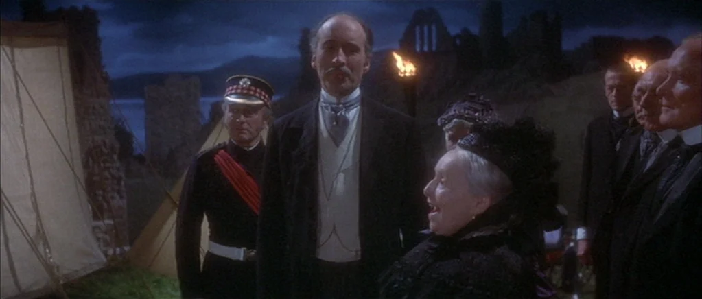 The Private Life of Sherlock Holmes movie still: medium — A group of 19th-century dignitaries gather outside at night near stone castle ruins. They…