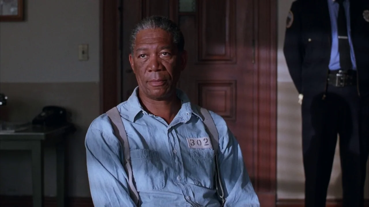 The Shawshank Redemption (1994) movie still: medium — An interior office with dark wood paneling and a worn desk in the background. An elderly man…