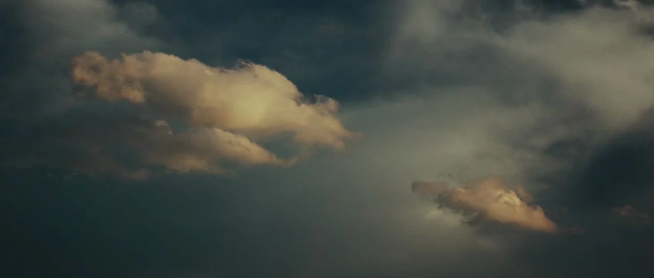 Meadowland (2015) movie still: establishing — A dark, overcast sky features dense storm clouds covering most of the frame. Golden light reflects off…