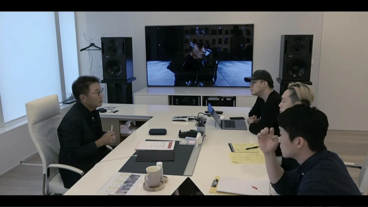 Lee Soo Man: King of K-Pop (2025) movie still: medium — A modern minimalist meeting room features a large white desk and high-end audio speakers.…