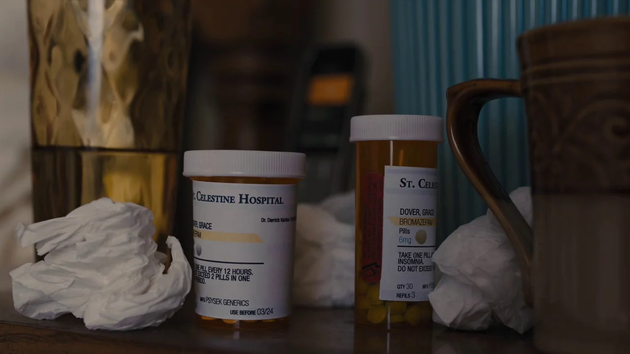 Prisoners (2013) movie still: closeup — Two amber pill bottles stand on a wooden surface surrounded by crumpled tissues. A dark mug sits on the…
