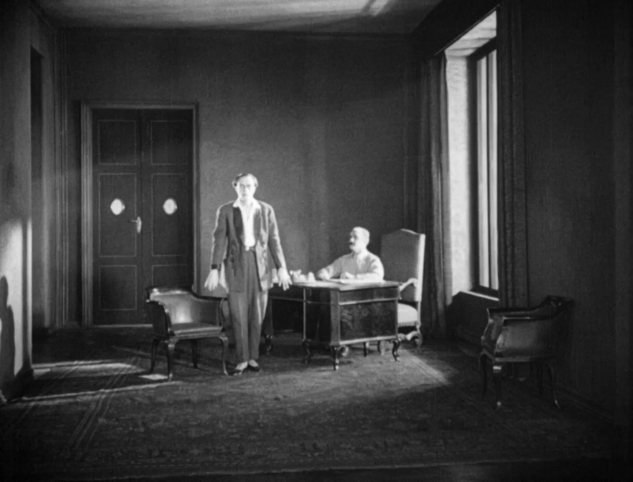 The Hands of Orlac (1924) movie still: fullbody — A spacious wood-paneled room features a heavy desk and leather chairs. A man stands in the middle…