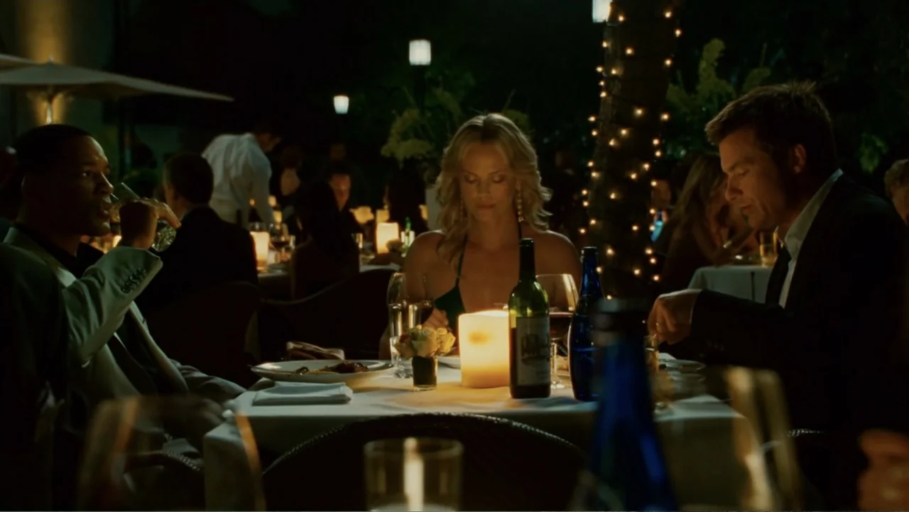 Hancock (2008) movie still: medium — An outdoor dining area at night features a table covered in white linen. Three people sit around the table…