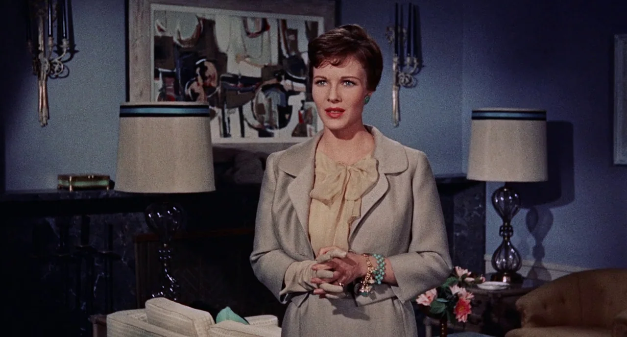 Bell Book and Candle (1958) movie still: medium — A refined mid-century living room features blue walls, table lamps, and abstract artwork. A woman…
