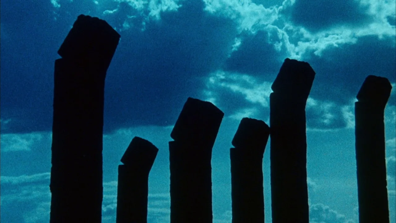 Phase IV (1974) movie still: wide — Ancient stone pillars stand against a dark, dramatic sky filled with scattered clouds. These crumbling monuments…