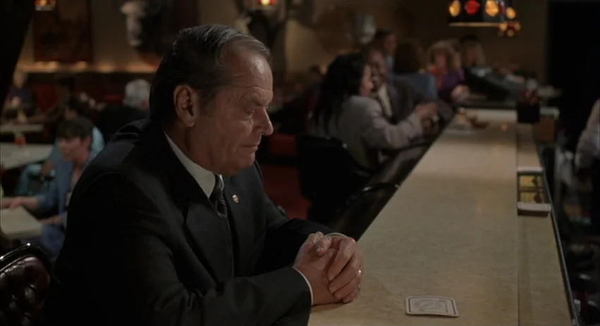 About Schmidt movie still: medium — A dimly lit lounge featuring a long bar with customers in the background. An elderly man in a suit sits at the…