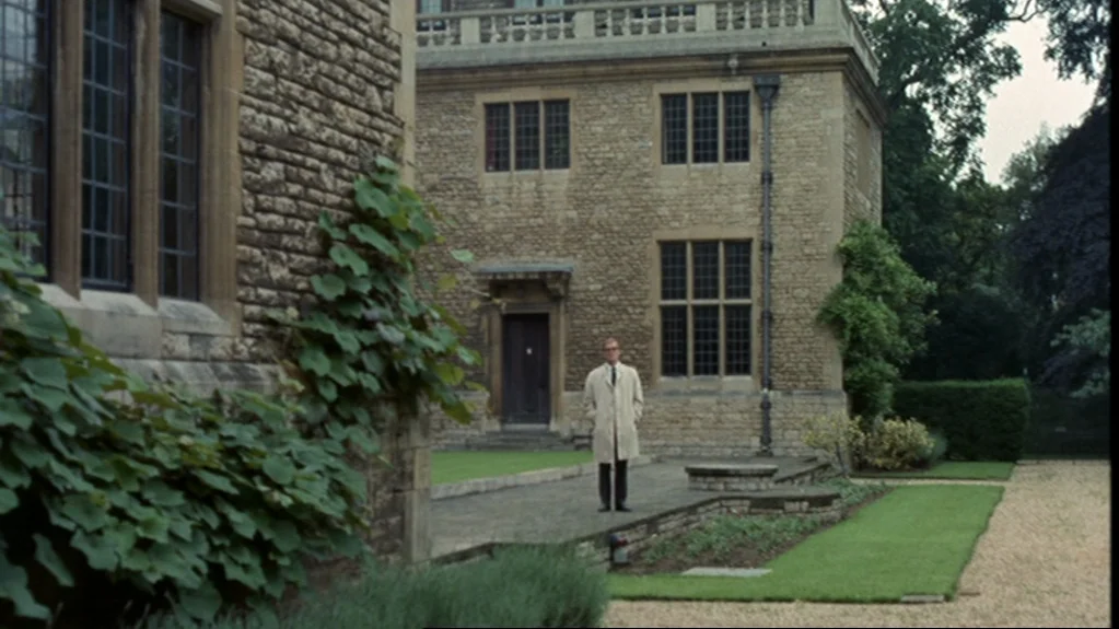Accident (1967) movie still: wide — A historic stone manor house features multi-pane grid windows and an ivy-covered facade. A solitary man stands…
