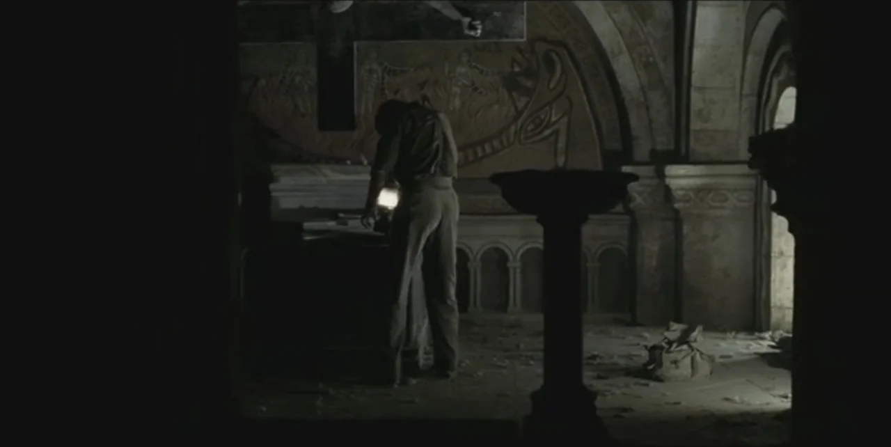 Exorcist: The Beginning (2004) movie still: fullbody — A dark stone crypt features arched alcoves and faded mural paintings on the wall. A man…