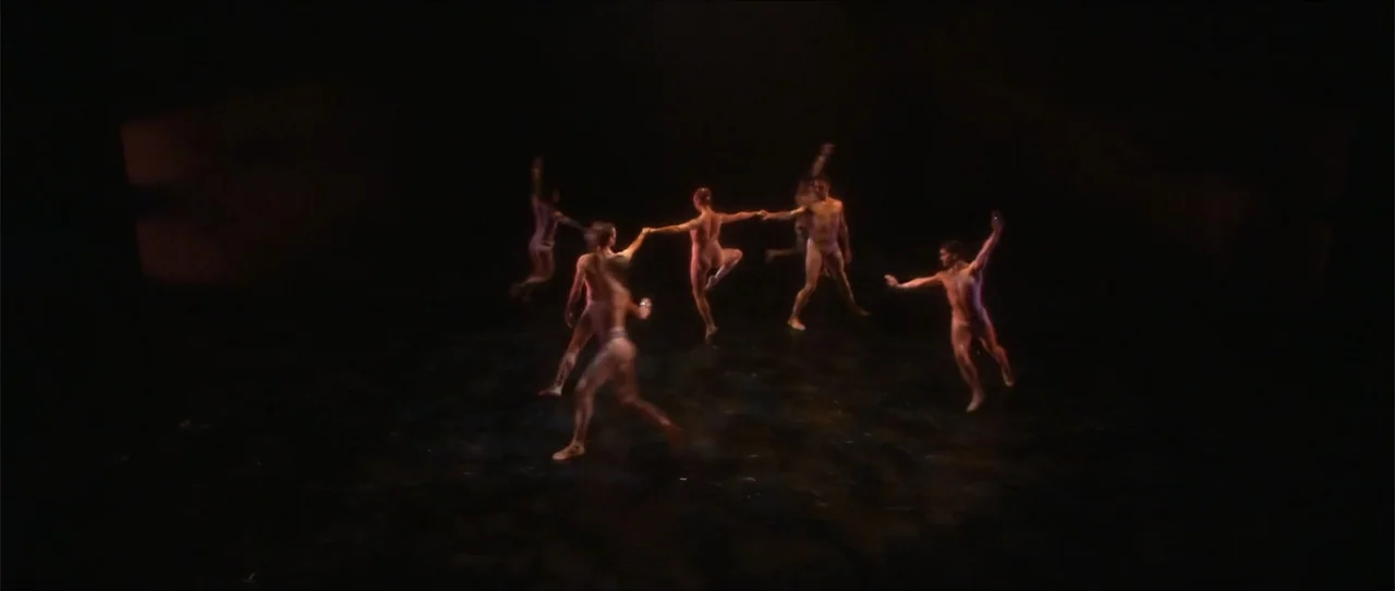 El acto (1989) movie still: wide — A large, dark performance stage contains six dancers moving in a circular formation. The performers wear…