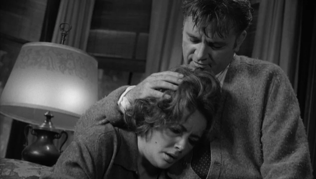 Who’s Afraid Of Virginia Woolf? (1966) movie still: medium — A dimly lit room features a table lamp with a patterned lampshade on the left. A man in…