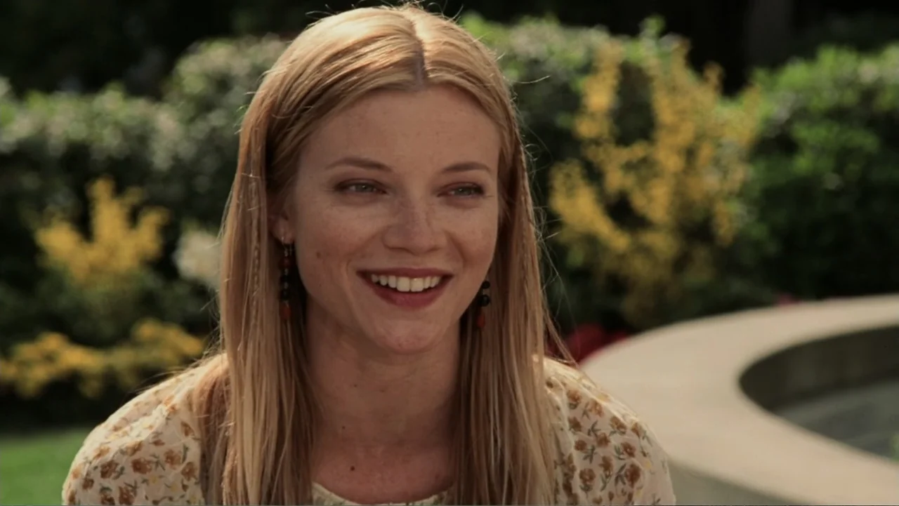The Butterfly Effect (2004) movie still: medium — A sunny garden features blurry green foliage and a concrete curb in the background. A young woman…