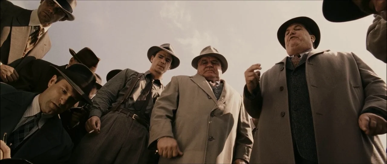 The Black Dahlia (2006) movie still: wide — A group of men in fedoras and vintage suits cluster tightly together outdoors. They stand over the…