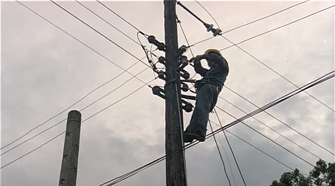 A Time To Love and A Time To Die (1985) movie still: fullbody — An electrical worker climbs a wooden utility pole against an overcast, grey sky. The…