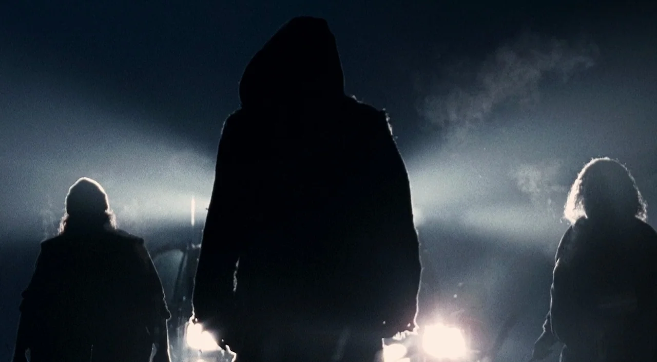 Halloween 2 (2009) movie still: fullbody — Three figures stand in the middle of a dark road at night. Bright headlights illuminate the scene from…