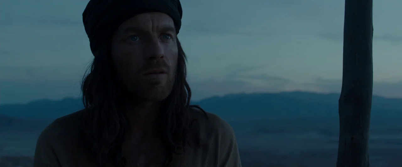 Last Days in the Desert (2015) movie still: medium — An arid landscape is visible behind a man during the blue hour. The man gazes forward while…