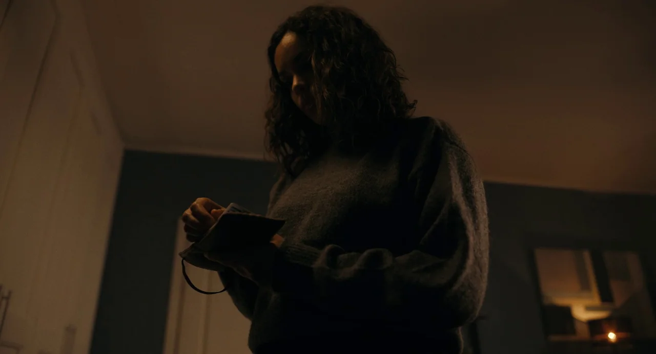 Barbarian (2022) movie still: medium — A dimly lit room with muted blue walls and white trim features a person. A woman in a dark grey knit sweater…