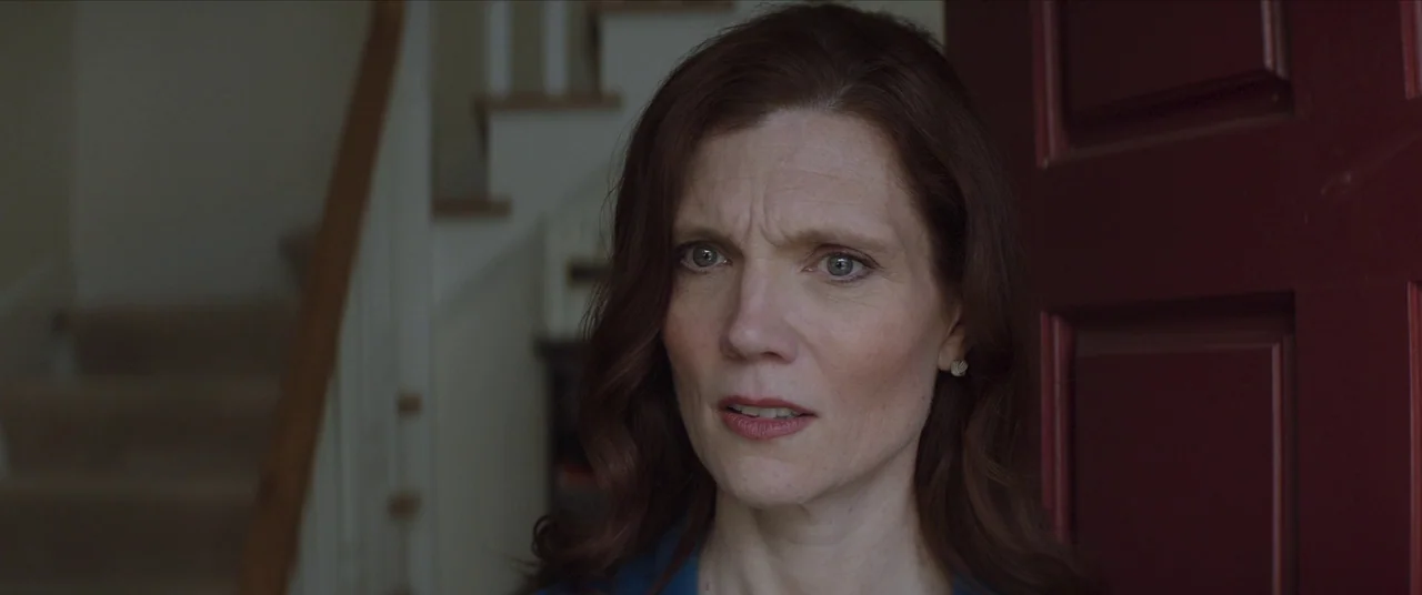 Thoroughbreds (2017) movie still: closeup — A residential entryway with a red door and wooden stairs visible in the background. A woman in a blue…