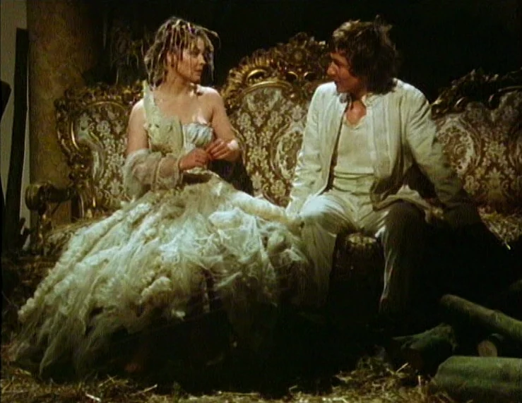 The Tempest (1979) movie still: medium — A dark space features a heavily ornate vintage sofa with patterned upholstery. A man and woman sit side by…