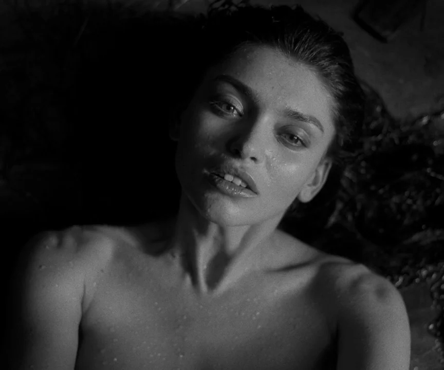 The Lighthouse (2019) movie still: closeup — A dark space with a damp surface and indistinct shadows. A young woman looks upward while lying down in…