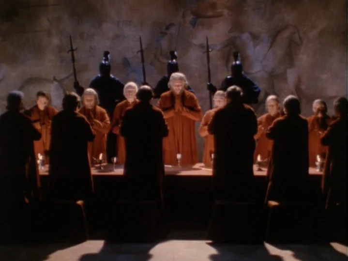 The Magic Flute (1975) movie still: wide — A dark stone hall features a wall with ancient relief carvings and standing guards. Twelve robed figures…