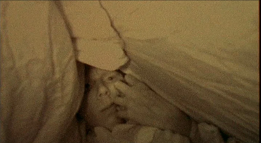 Julien Donkey Boy (1999) movie still: closeup — A close view of a person underneath layers of heavy, off-white fabric bedding. The subject is…