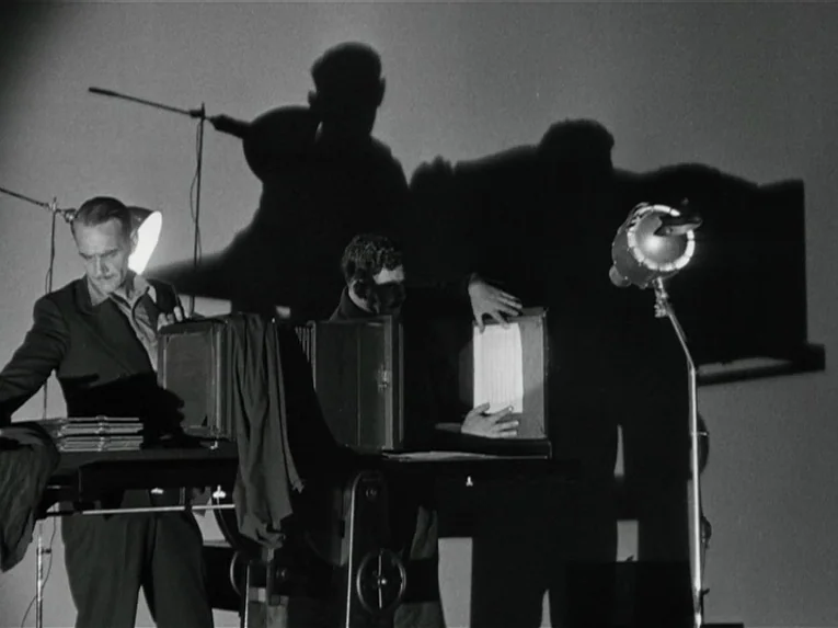 Mata Hari (1931) movie still: medium — A stark room features two men working at a large photo reproduction camera station. They manipulate documents…