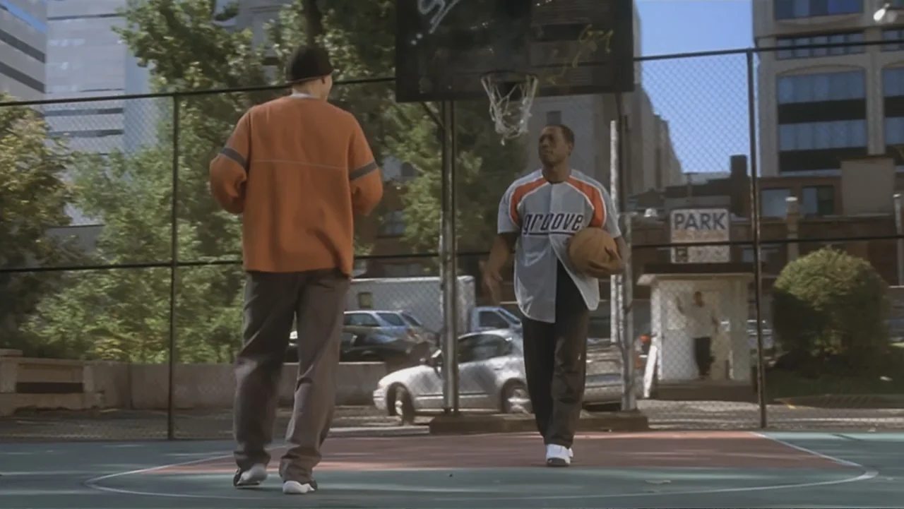 The Art of War (2000) movie still: fullbody — An urban outdoor basketball court features chain-link fencing and city buildings in the background.…