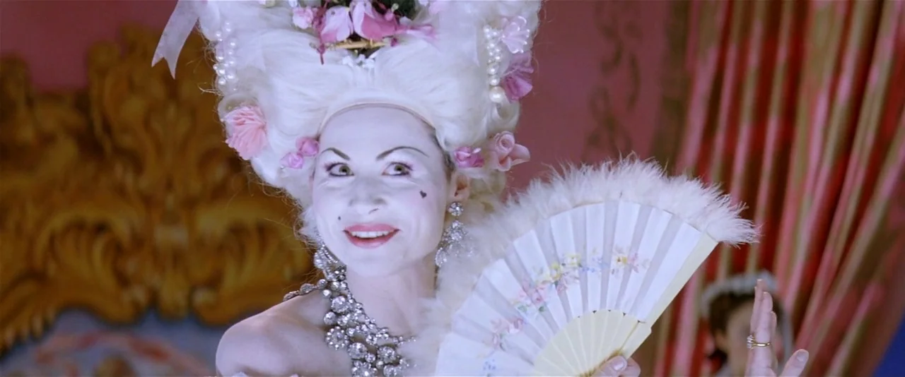 The Phantom of the Opera (2004) movie still: medium — An opulent room with gilded wood carvings and pink curtaining background features. A woman in…