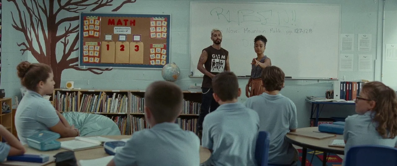 Sound of Metal (2019) movie still: wide — An elementary classroom features a math wall display and a whiteboard with written assignments. A man and…