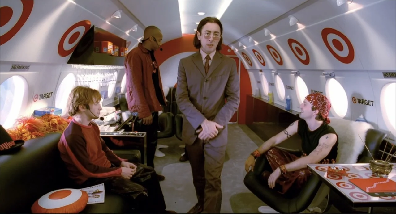 Josie and the Pussycats (2001) movie still: fullbody — A modern airplane cabin features white curved walls decorated with red target logos. A man in…