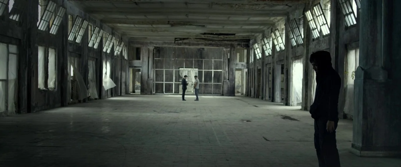 The Raid 2 (2014) movie still: wide — A vast, abandoned interior space features tiled floors, large windows, and aged industrial columns. A man in a…