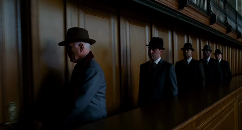 The Adjustment Bureau (2013) movie still: wide — A long hallway features dark, paneled wood walls and a high-set metal grille. Five men wearing…