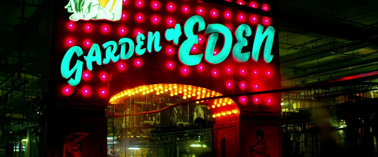 Pain & Gain (2013) movie still: wide — A dark industrial-style interior houses a large illuminated sign with red bulbs and cyan letters. The sign…