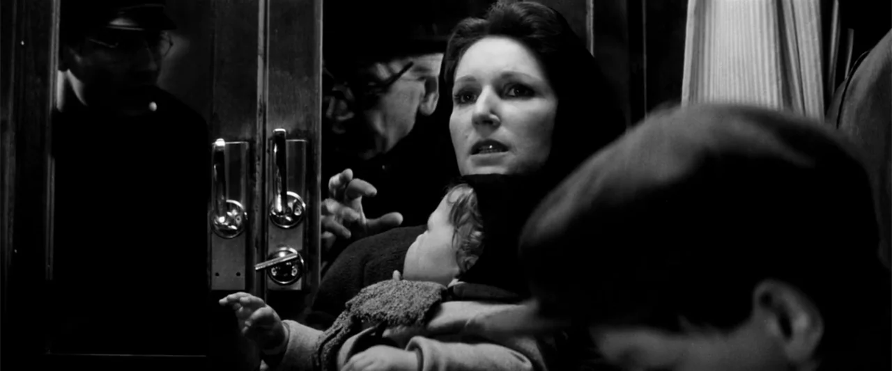 Europa (1991) movie still: medium — The interior of a crowded passenger train at night featuring wood paneling. A woman looks off-camera while…