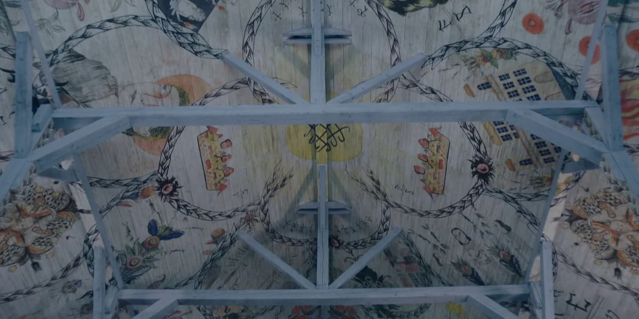 Midsommar (2019) movie still: establishing — A wooden ceiling features intricate folk art paintings depicting circular wreaths and symbols. Support…