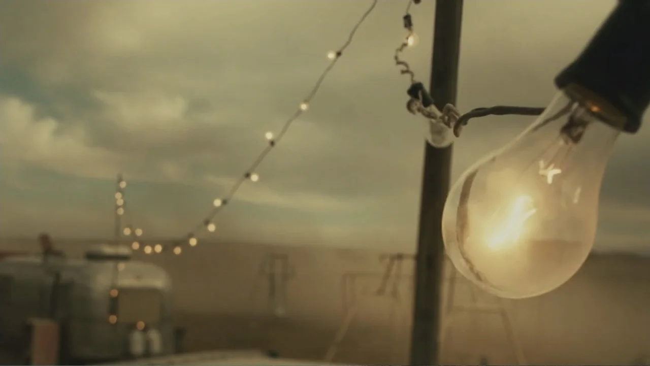 Legion (2010) movie still: closeup — An outdoor desert location features a string of lights hanging above a silver trailer. The glowing bulbs…