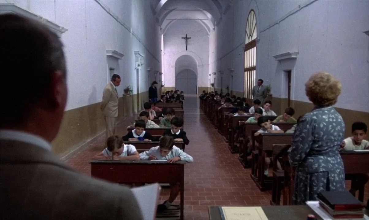 Cinema Paradiso (1988) movie still: wide — A long, narrow school room features high vaulted white ceilings and rows of desks. Students sit at the…