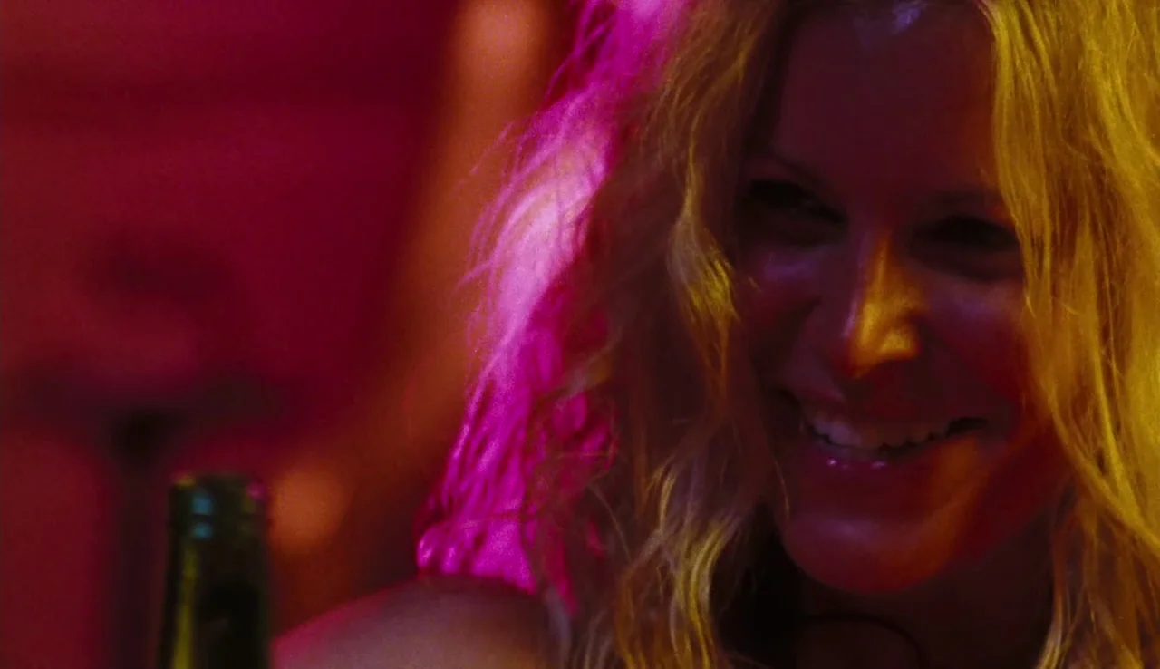 The Devil’s Rejects (2005) movie still: closeup — A dimly lit space features intense pink and yellow neon lighting reflecting off surfaces. A blonde…