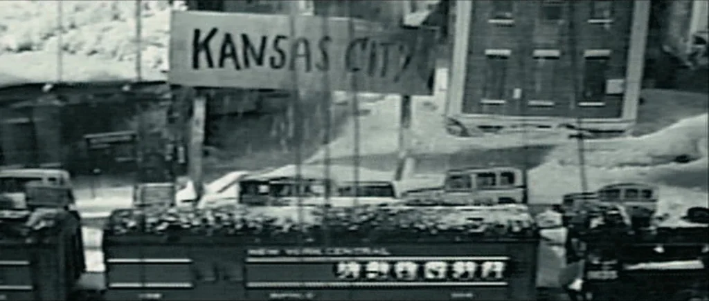 Be Kind Rewind (2008) movie still: wide — A bustling railway platform features a large sign labeled Kansas City overhead. A New York Central train…