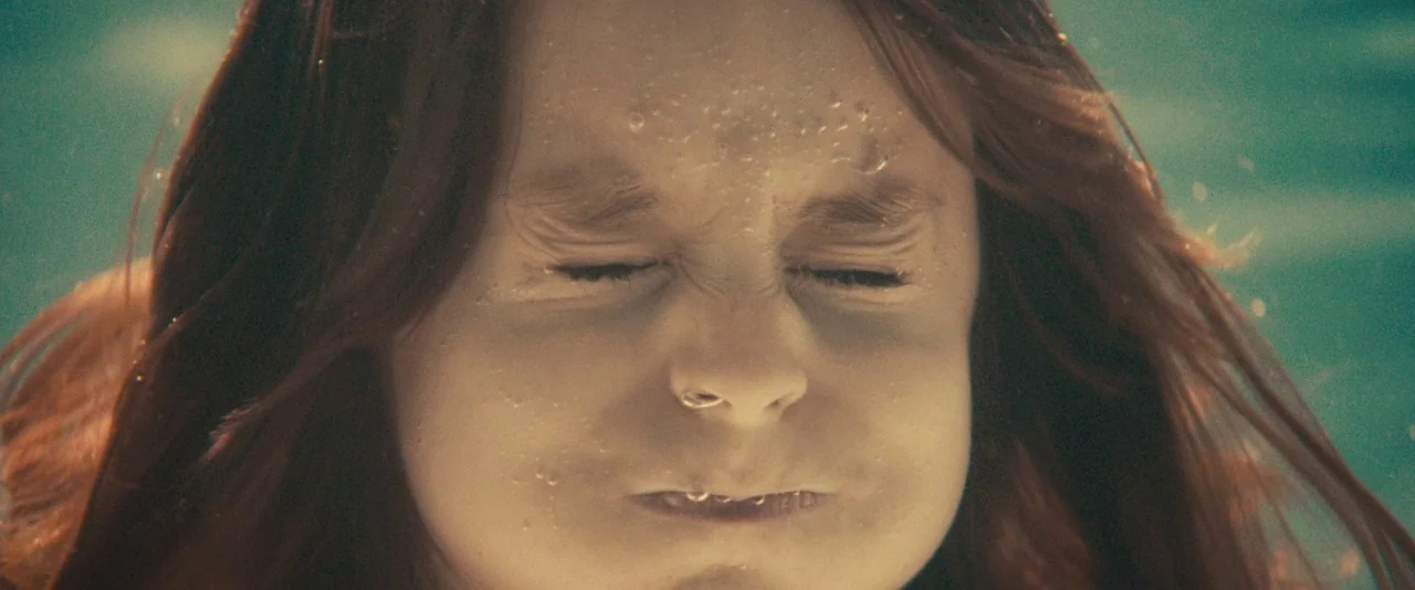 The Skeleton Twins (2014) movie still: closeup — A young girl is submerged in clear water with her face near the camera. She keeps her eyes tightly…