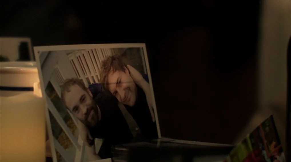 Your Sister’s Sister (2011) movie still: closeup — A close-up shot of a photograph resting on a dark, dimly lit surface. The photo depicts two young…