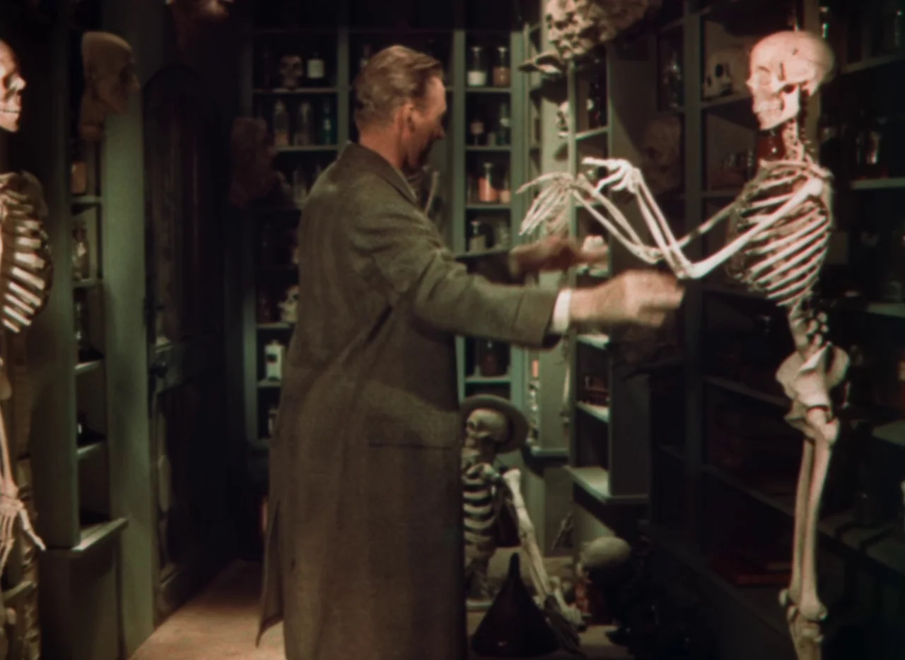 Doctor X (1932) movie still: medium — A cramped laboratory filled with anatomical specimens, including multiple skeletons and shelves of glass jars.…