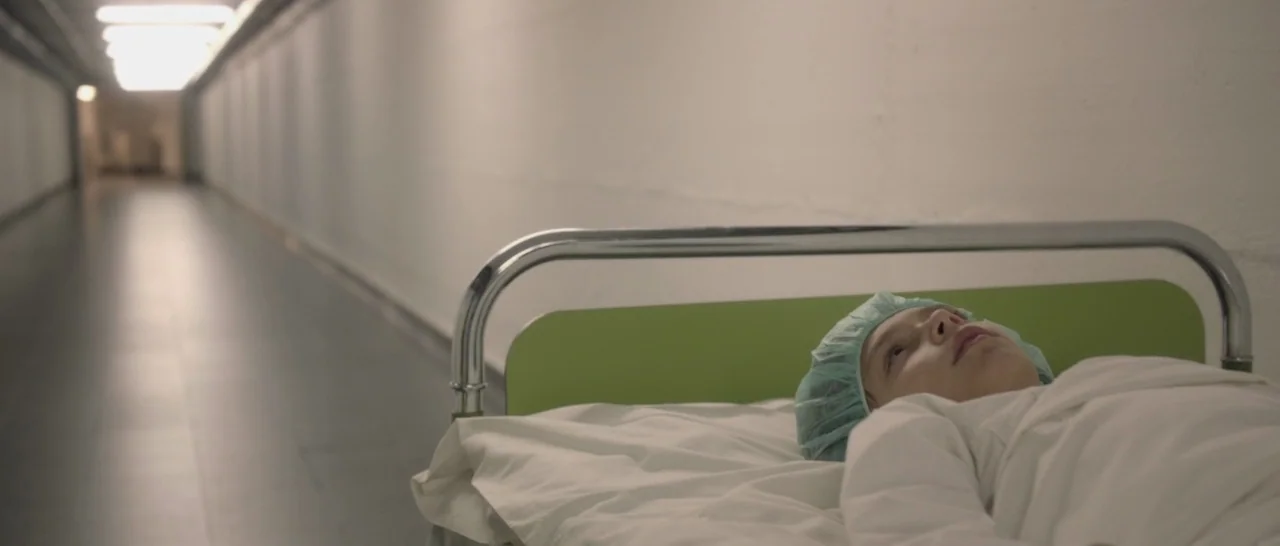 Nymphomaniac Vol 1 (2013) movie still: medium — A long, white, sterile hospital corridor stretches into the distance with bright overhead lighting.…
