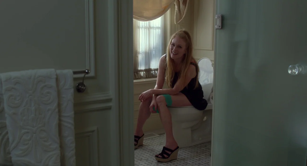 Maps to the Stars (2014) movie still: medium — A residential bathroom with tiled flooring and a window covered by translucent curtains. A woman sits…